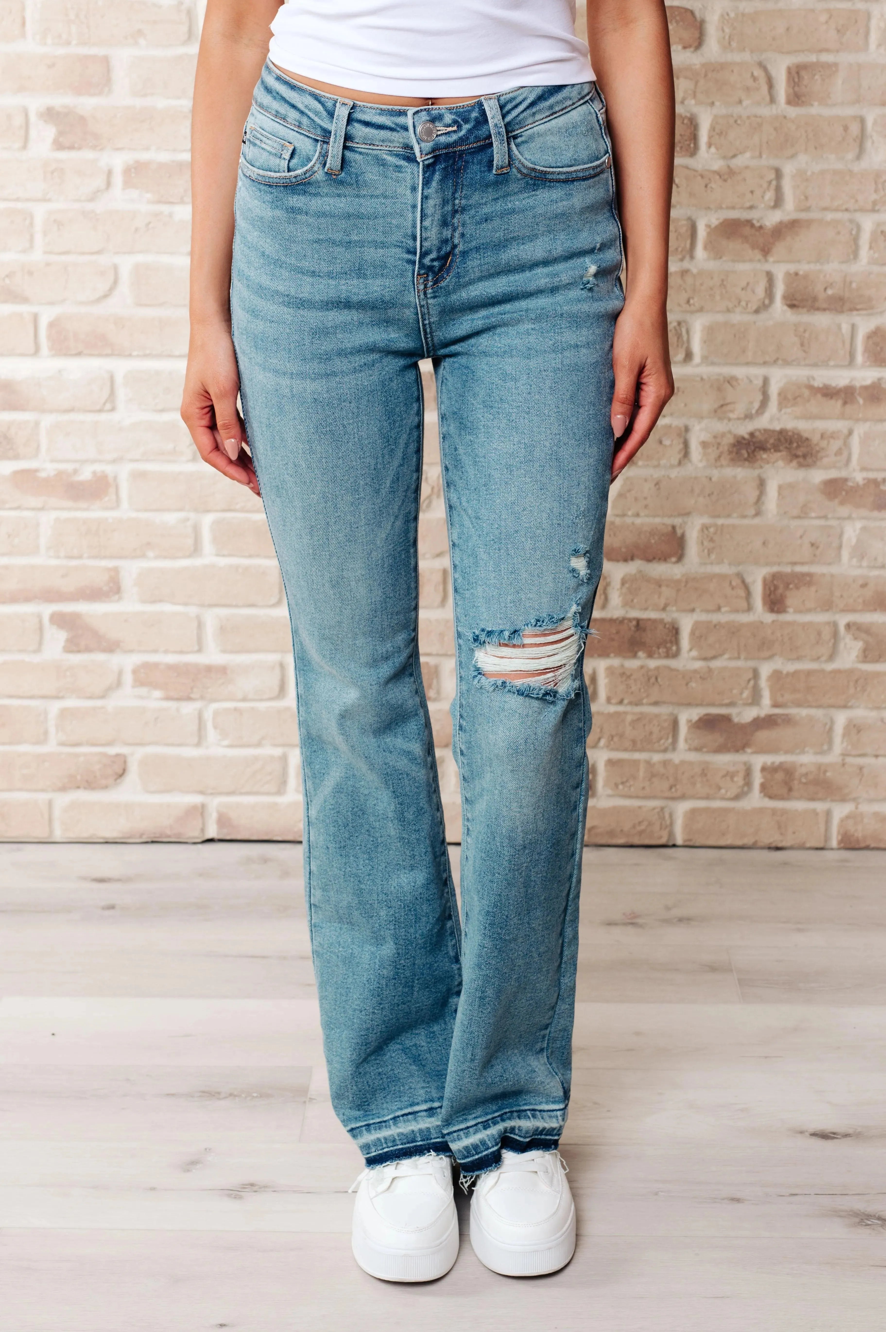 Model in Isla Mid Rise Distressed Released Hem Bootcut Jeans standing outdoors