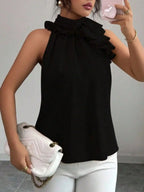 Woman wearing sleeveless black ruffle blouse with white pants and holding quilted clutch