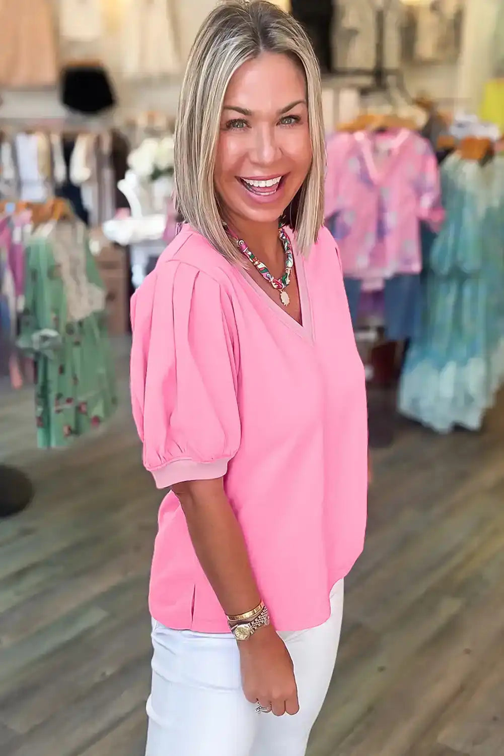 Woman wearing a pink puff sleeve blouse and white pants in a boutique clothing store