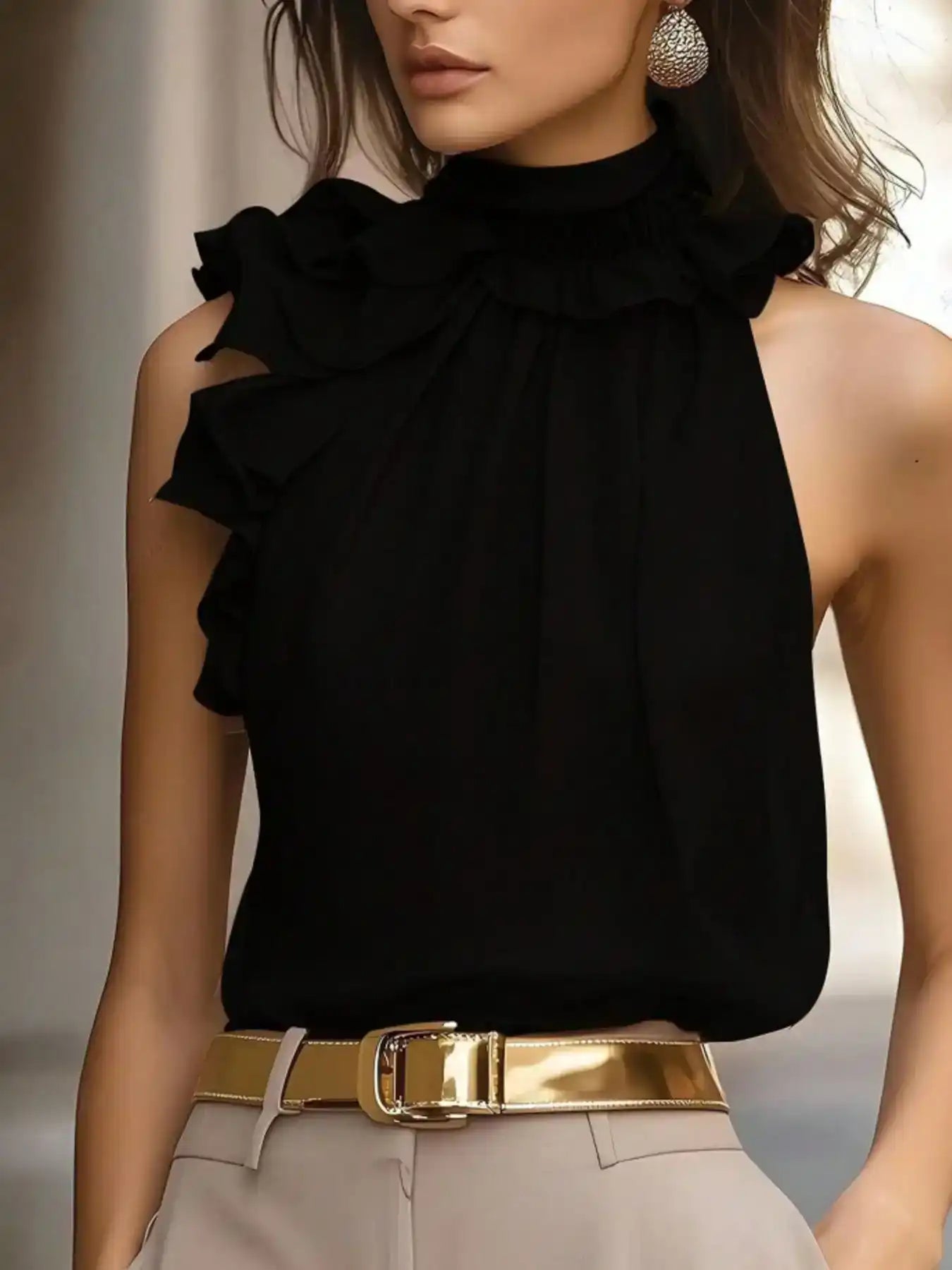 Woman wearing black ruffled sleeveless blouse, beige trousers, gold belt, and statement earrings