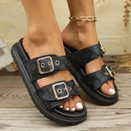Black double strap sandals with silver buckles on woman's feet, wood floor background