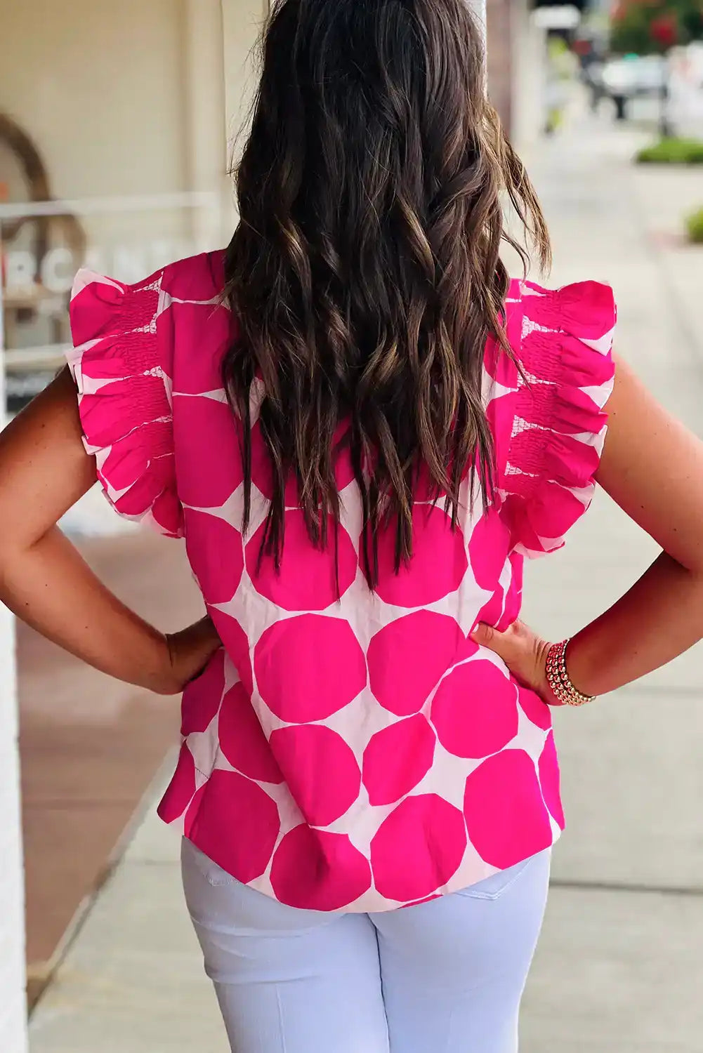 Woman wearing a pink polka dot ruffle sleeve blouse and white jeans outdoors