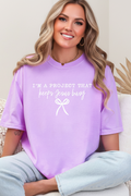 Person wearing a purple t-shirt with text and a bow graphic, sitting on a couch.