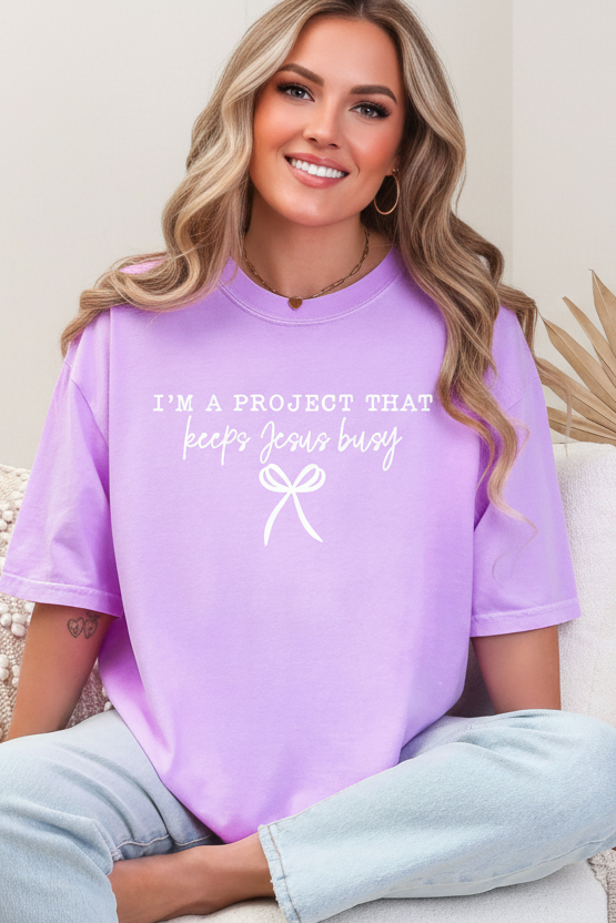 Person wearing a purple t-shirt with text and a bow graphic, sitting on a couch.