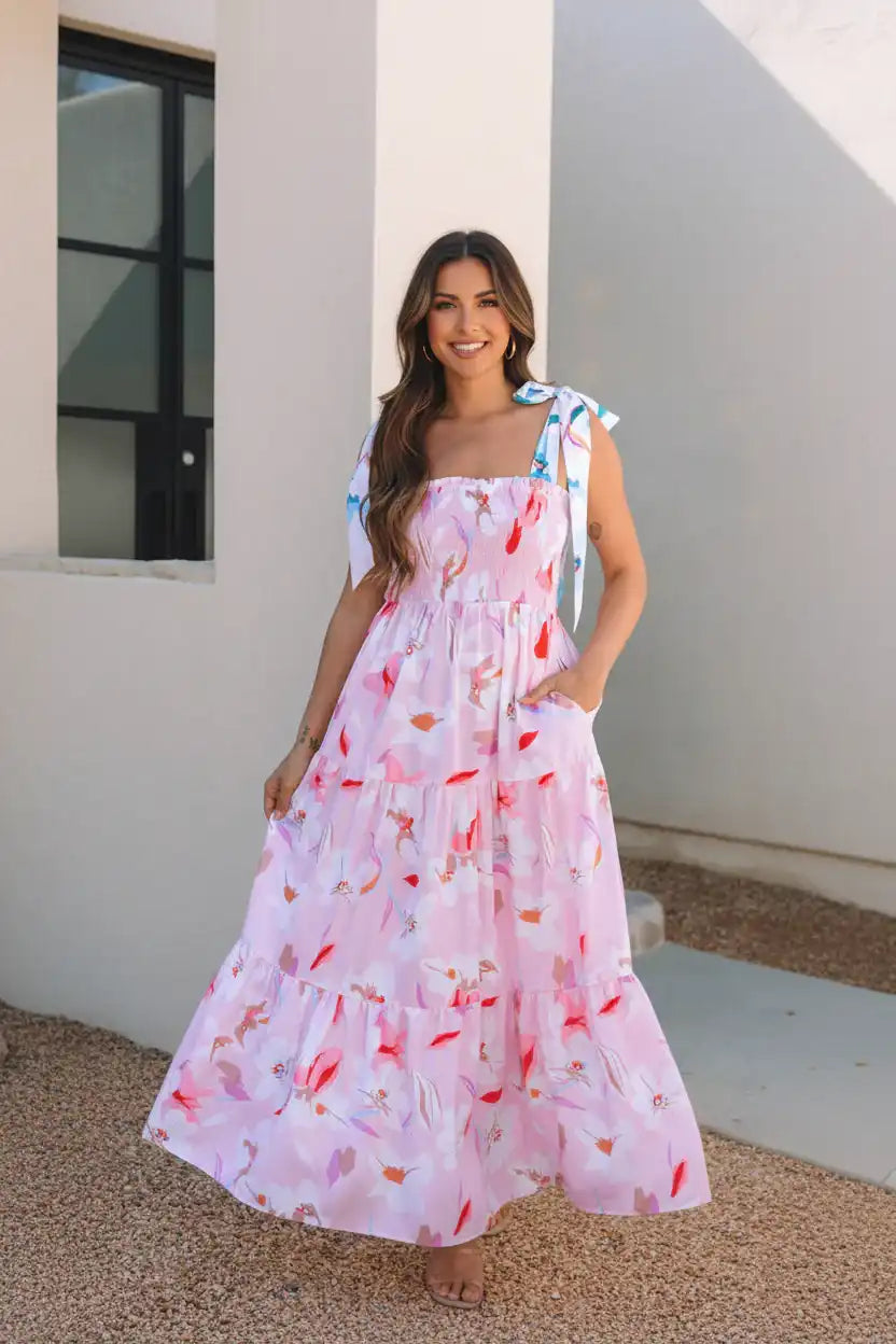 Woman wearing a floral dress standing against a light-colored wall.