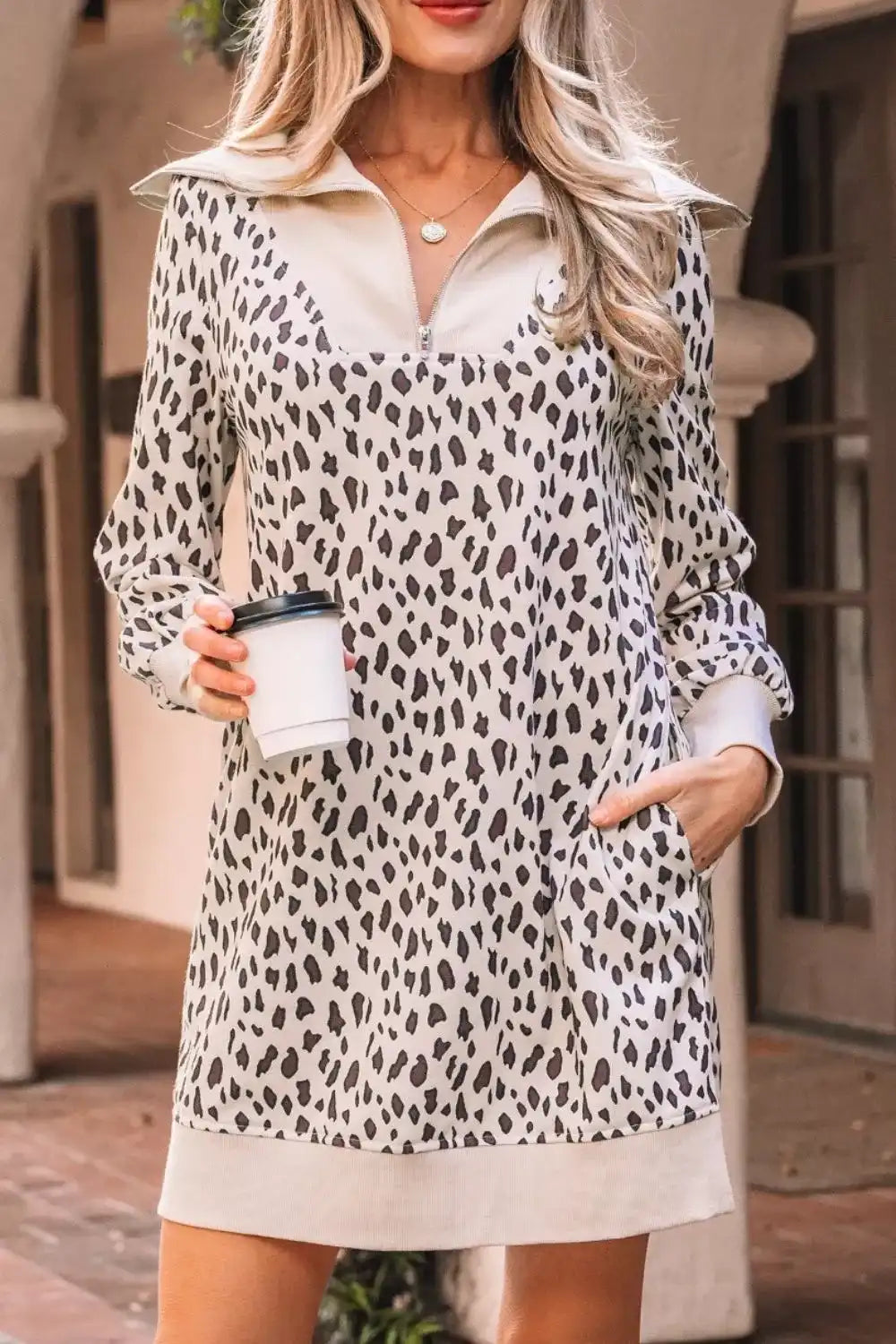 Woman wearing a long sleeve leopard print mini dress with pockets, holding a coffee cup