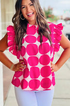 Woman wearing a pink polka dot ruffle sleeve blouse and white pants, smiling outdoors.