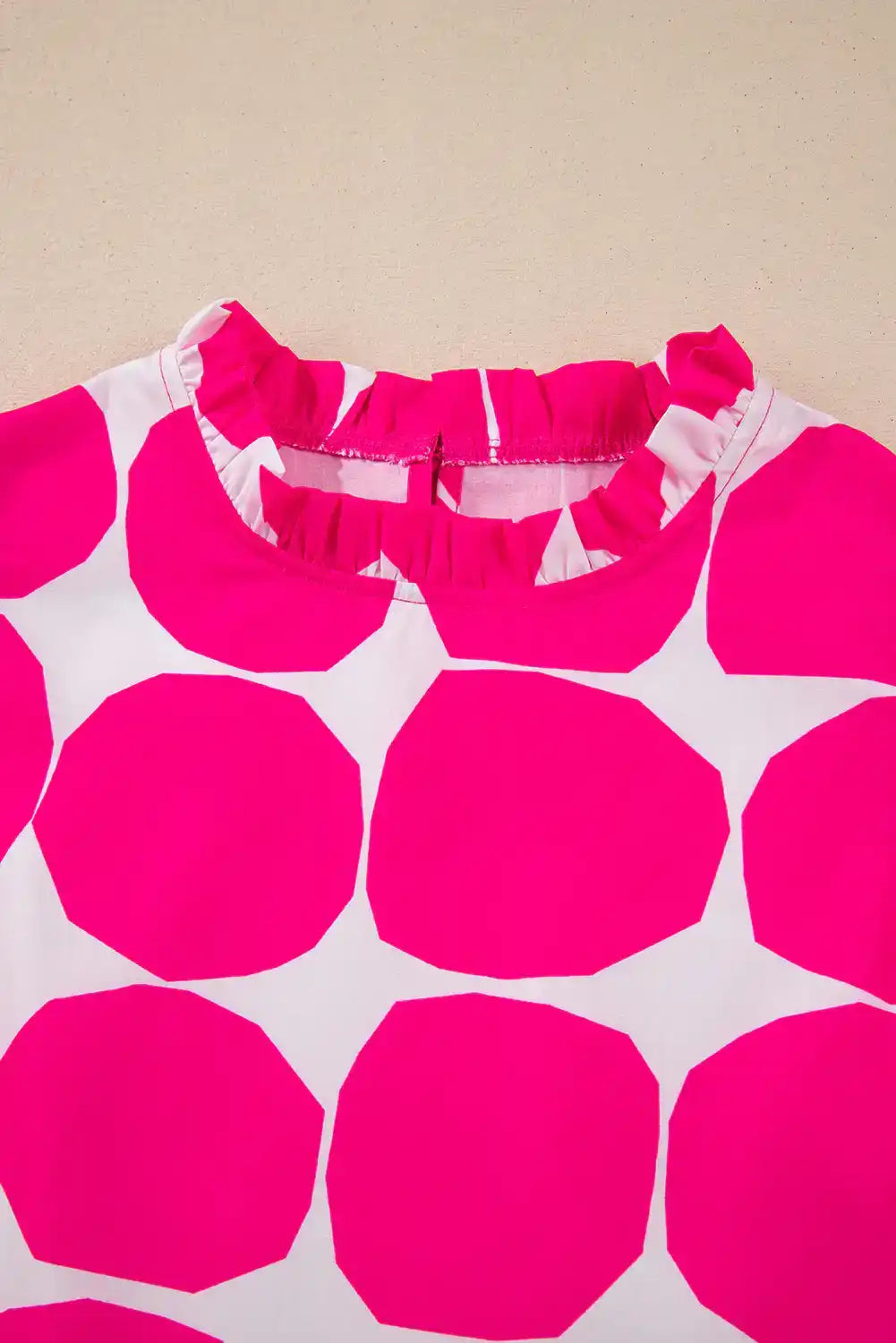 Close-up of pink polka dot women's blouse with ruffle collar on beige background