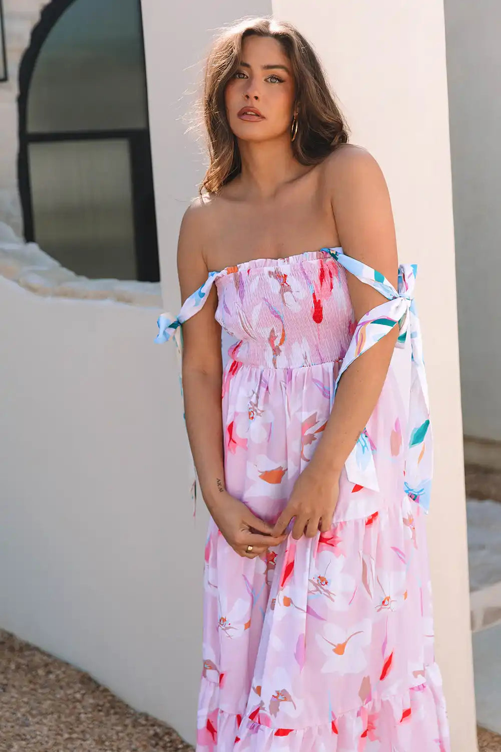 Woman wearing a floral off-shoulder dress against a white wall.