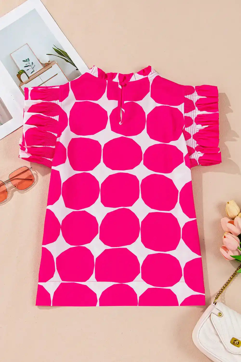 Pink and white polka dot women’s top with ruffled sleeves on beige background