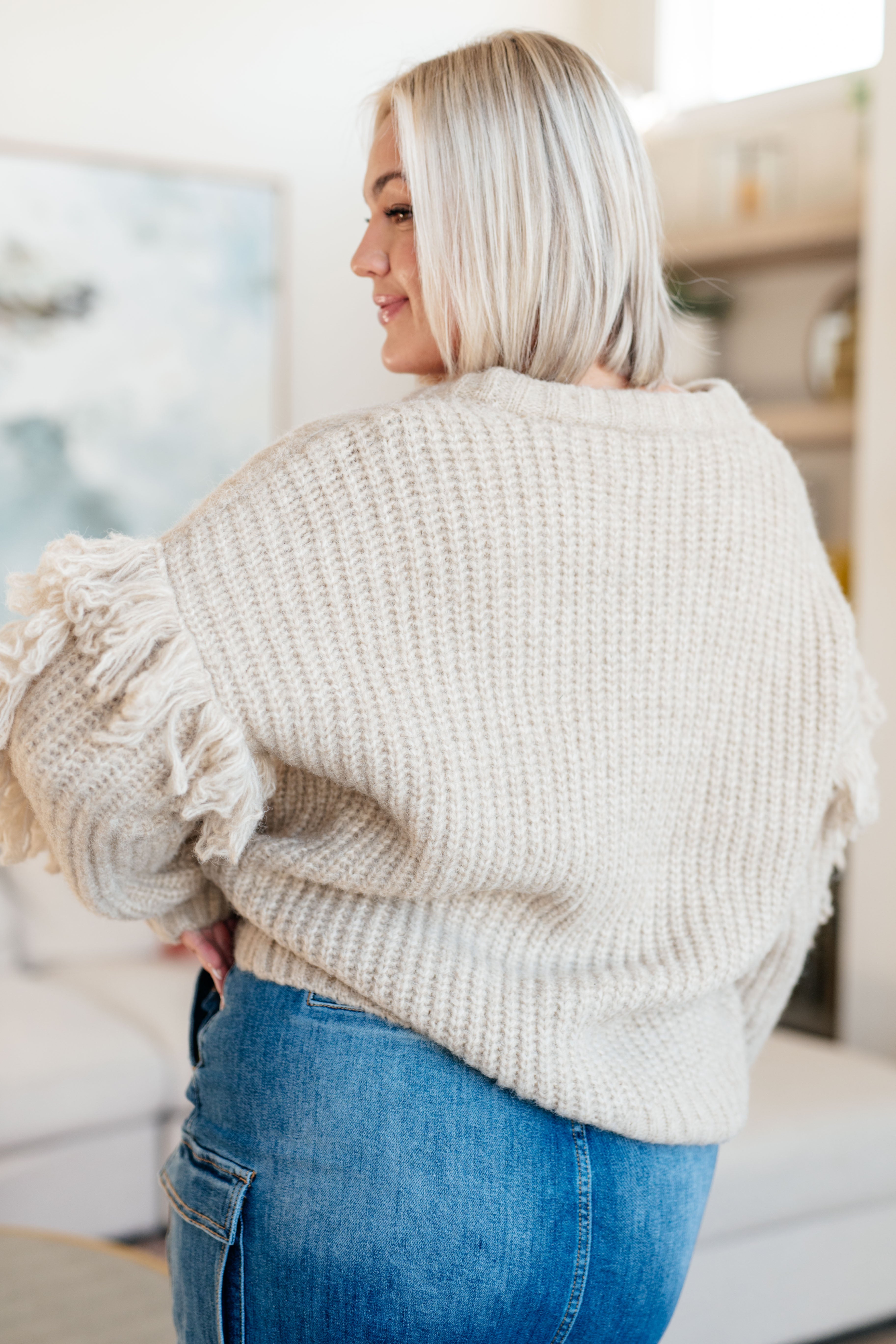 Woman wearing a beige knitted sweater and blue jeans in an indoor setting
