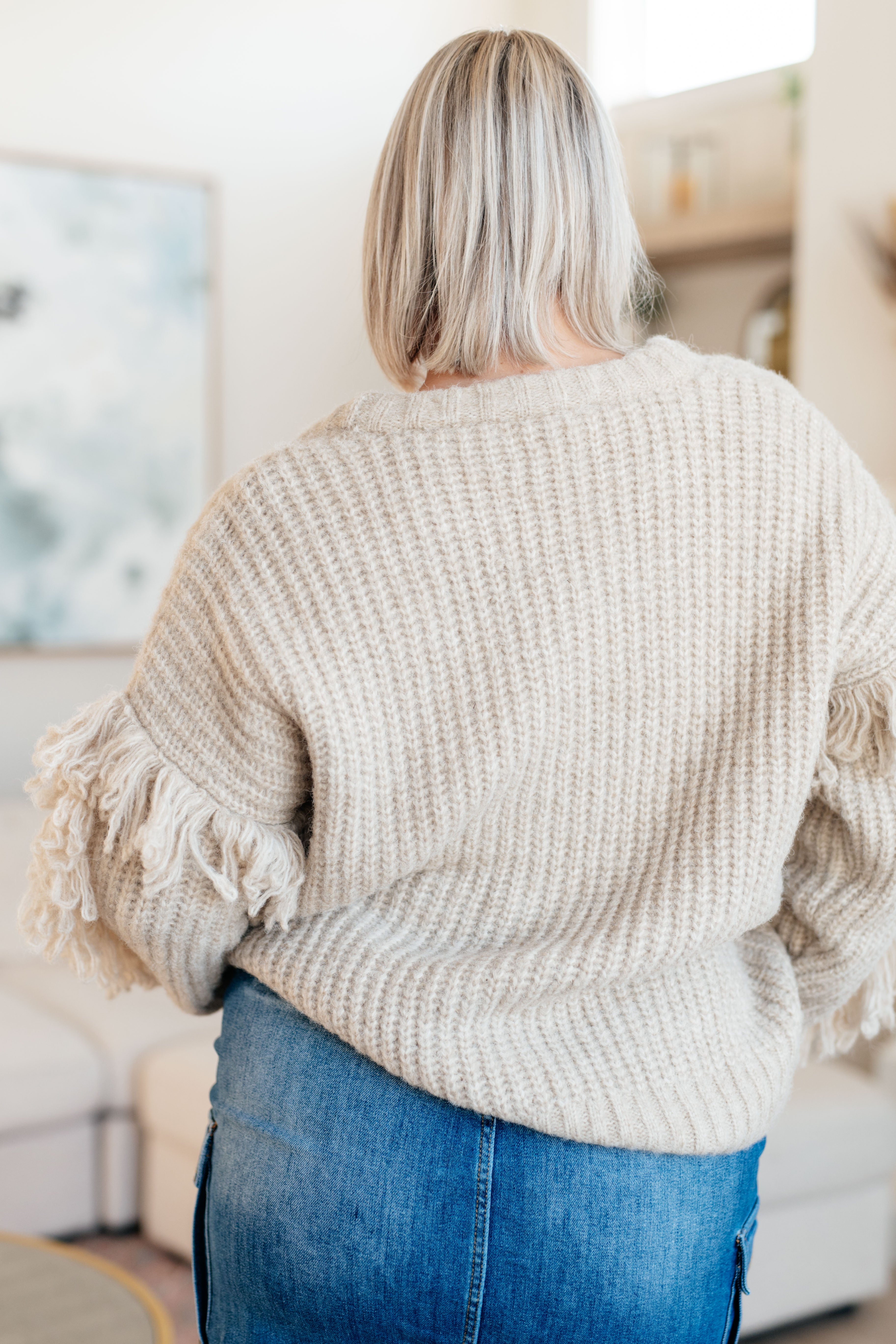 Person wearing a beige knitted sweater with tassel details in an indoor setting