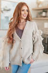 Woman wearing a beige cardigan with tassels in a cozy living room.