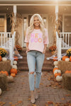 Woman standing in front of a house decorated for Halloween with pumpkins and hay bales.