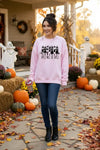 Woman in a pink sweatshirt standing in front of a decorated house for Halloween.