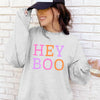 Person wearing a gray sweatshirt with 'HEY BOO' text in colorful letters against a brick wall.