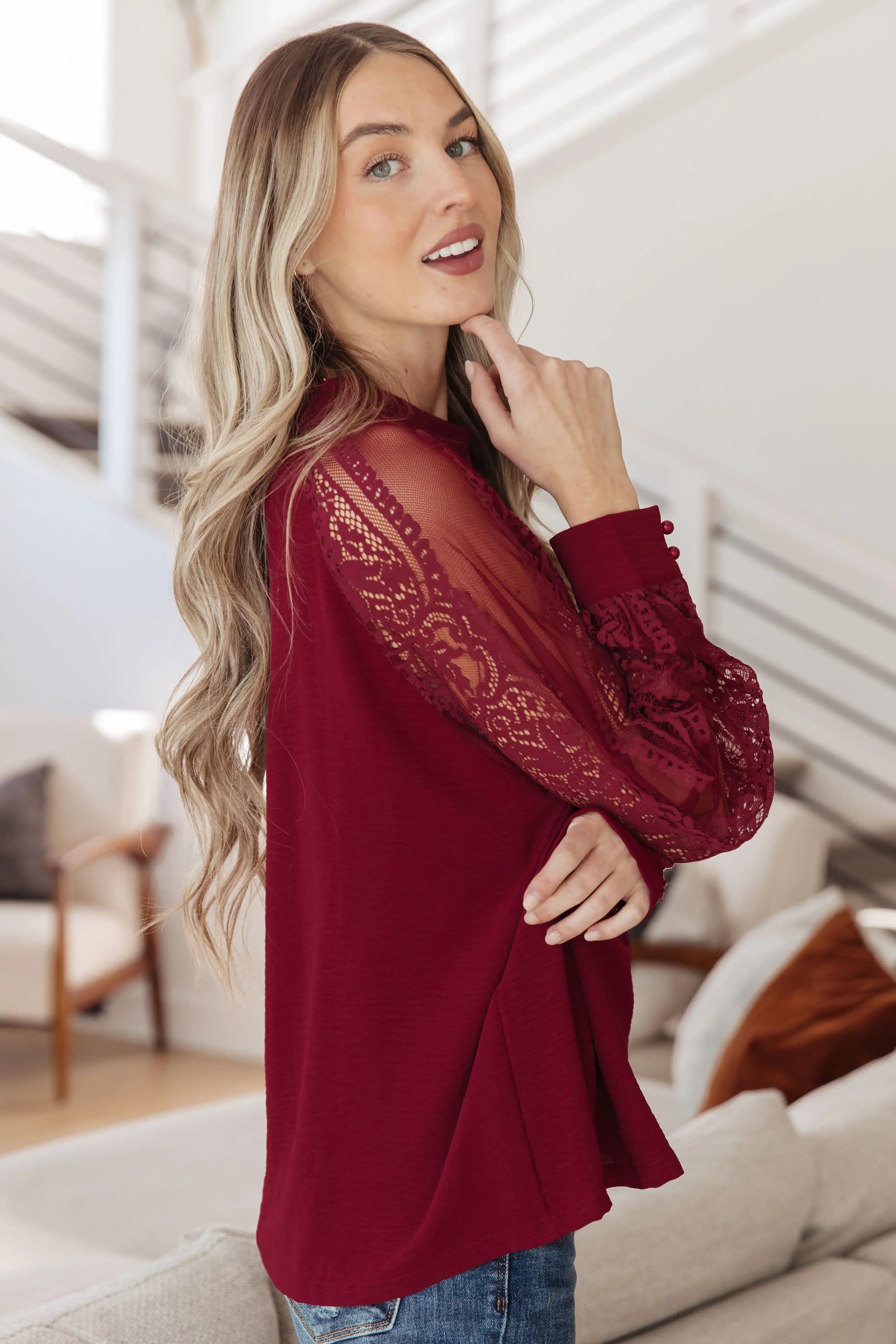 Woman wearing a burgundy blouse with lace sleeves in a living room setting