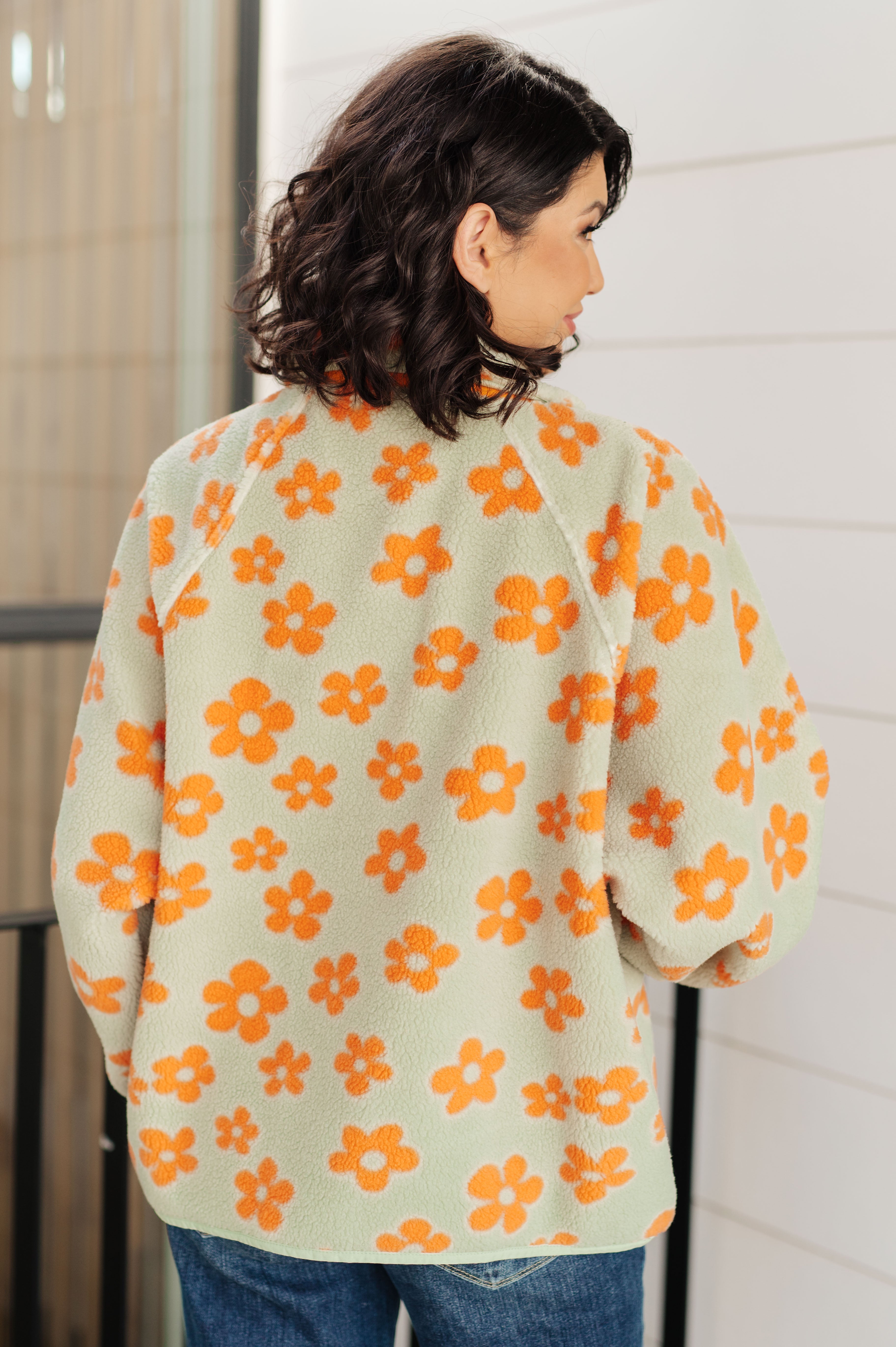 Person wearing a light green cardigan with orange floral patterns against a neutral background
