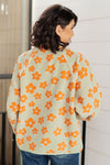 Person wearing a light green cardigan with orange floral patterns against a neutral background