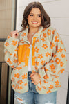 Woman wearing a floral jacket with orange flowers, yellow shirt, and blue jeans.
