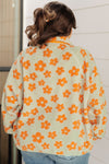 Person wearing a light-colored jacket with orange floral patterns against a white wall.