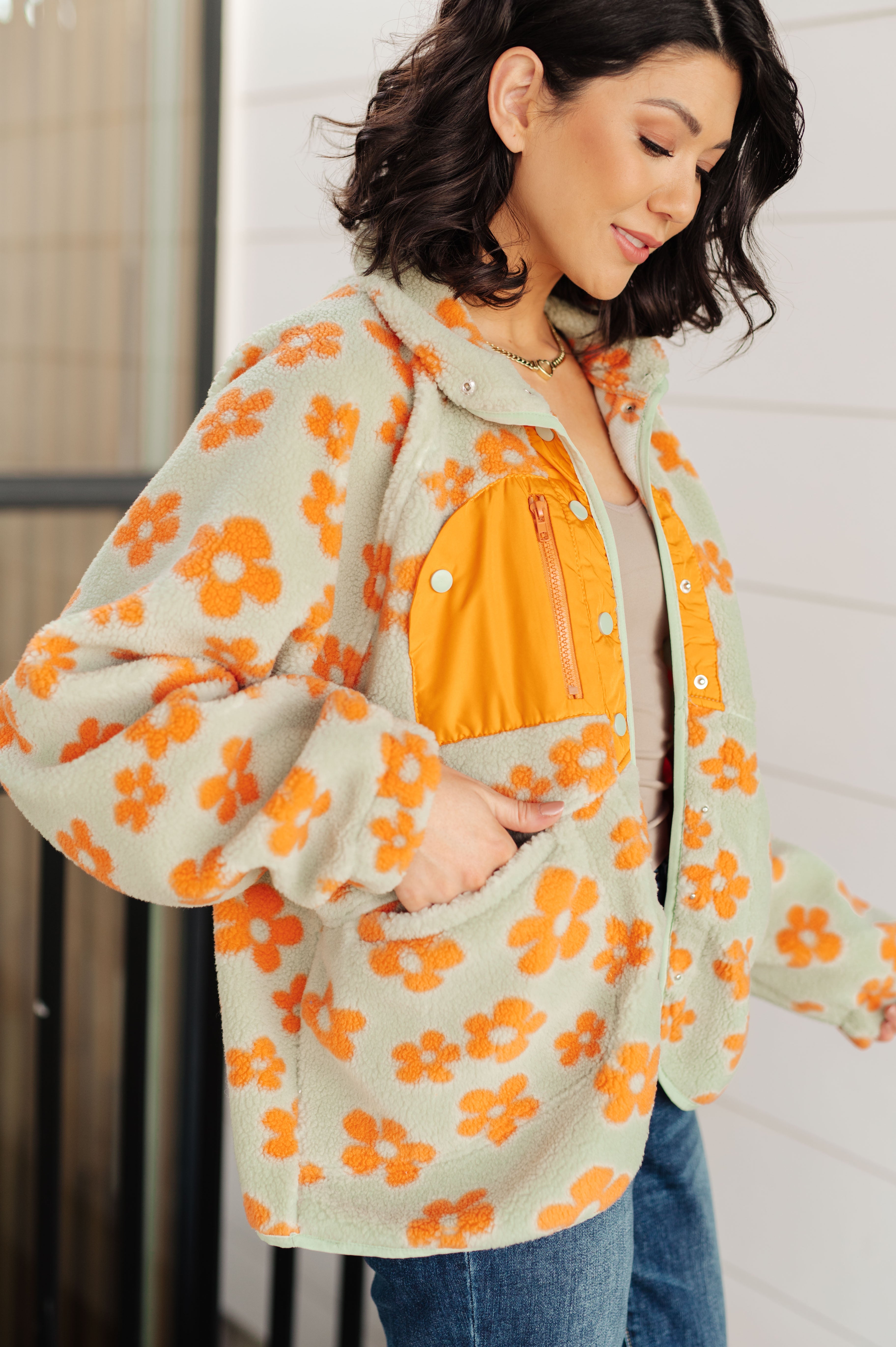 Woman wearing a floral jacket with orange flowers and a yellow shirt underneath.