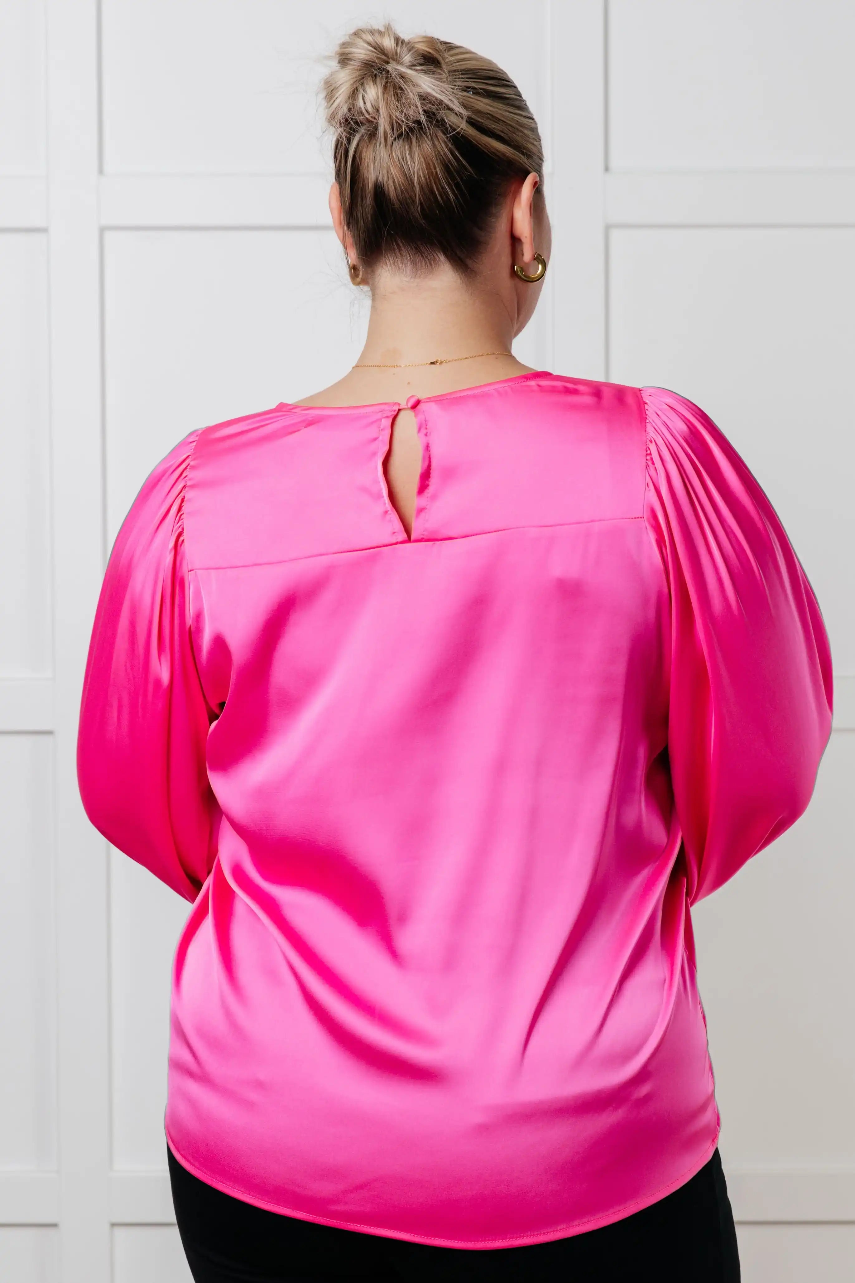 Person wearing a bright pink blouse with balloon sleeves against a white tiled wall.