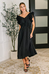 Woman wearing a black striped dress with ruffled shoulders in an indoor setting.