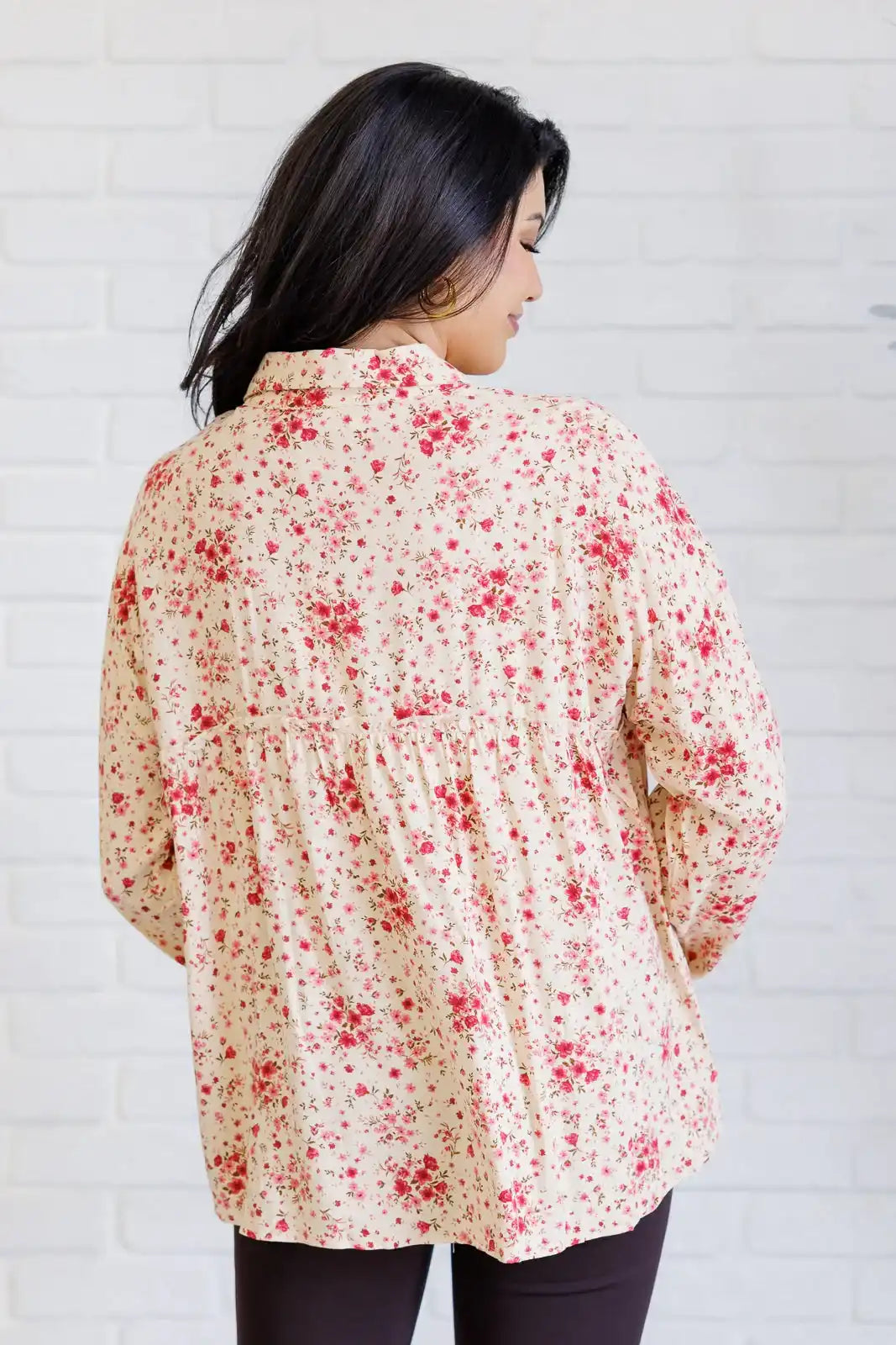 Woman wearing a floral blouse against a white brick wall