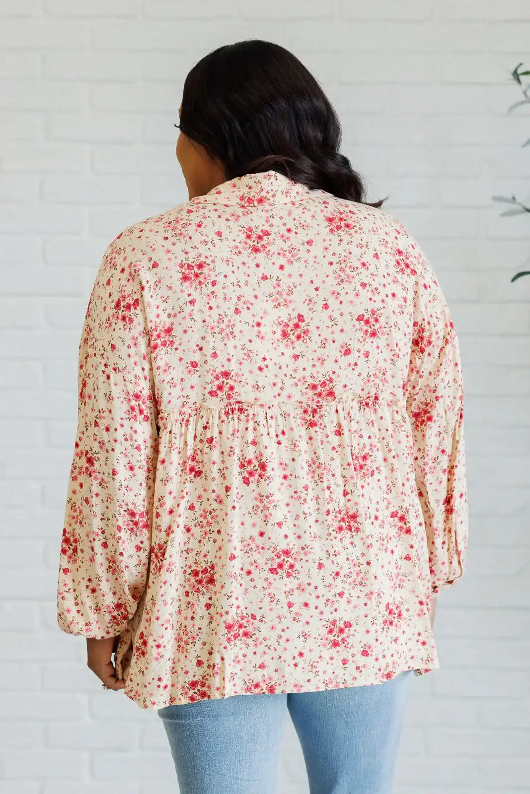 Person wearing a floral blouse with a white brick wall background