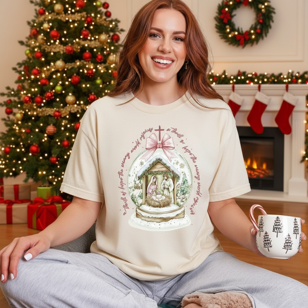 Woman wearing a Christmas-themed t-shirt with a nativity scene design, holding a mug, in a festive living room.