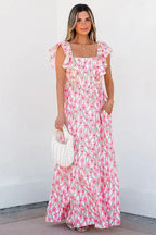 Woman in a pink floral maxi dress with ruffle sleeves holding a white handbag