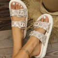 Women's beige double buckle sandals with patterned straps, white soles, and pedicured toes