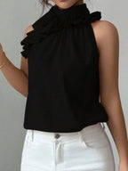 Woman wearing a sleeveless black ruffle mock neck blouse with white jeans