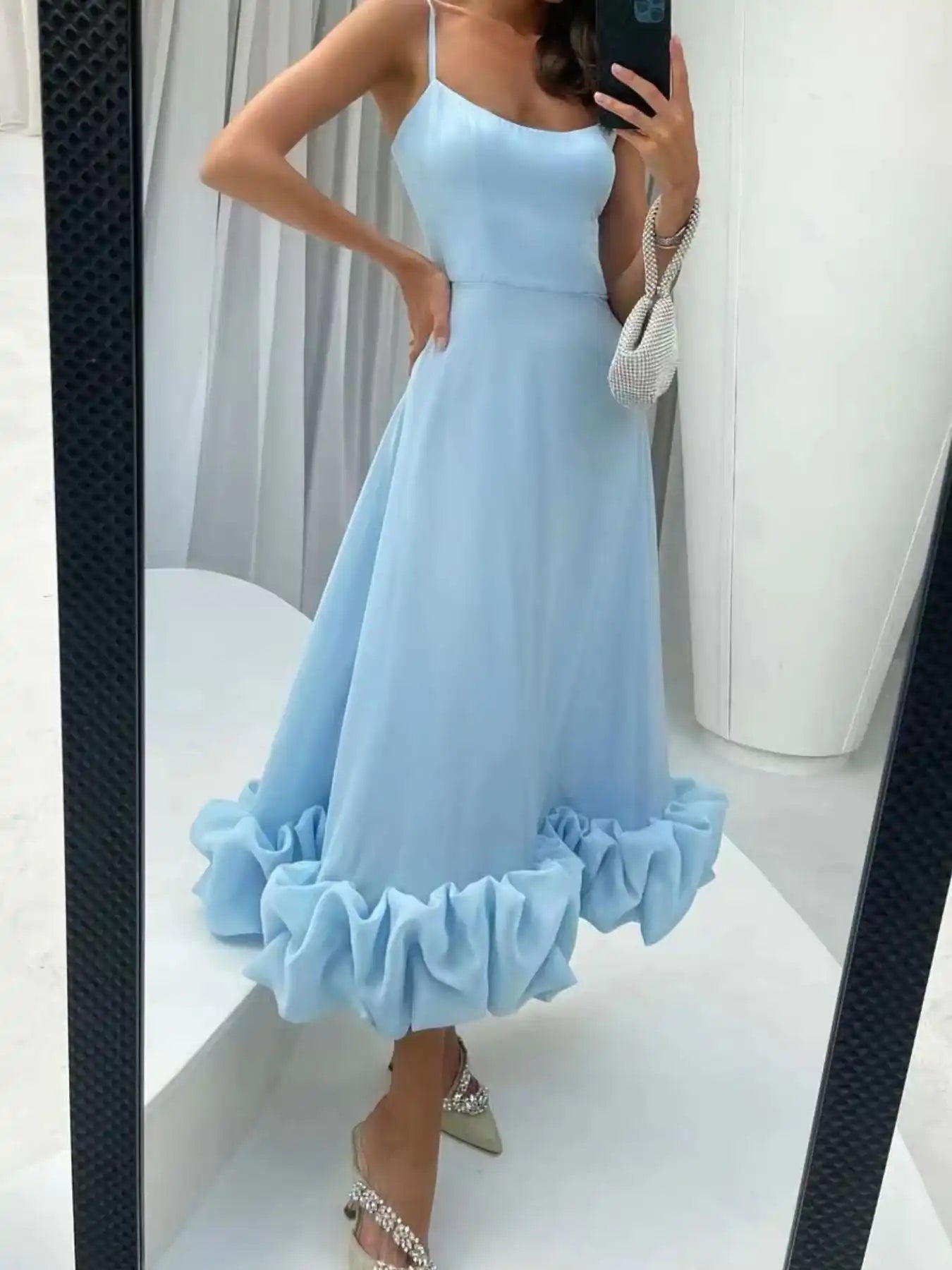 Light blue ruffle hem midi dress with spaghetti straps, paired with embellished heels and a beaded bag.