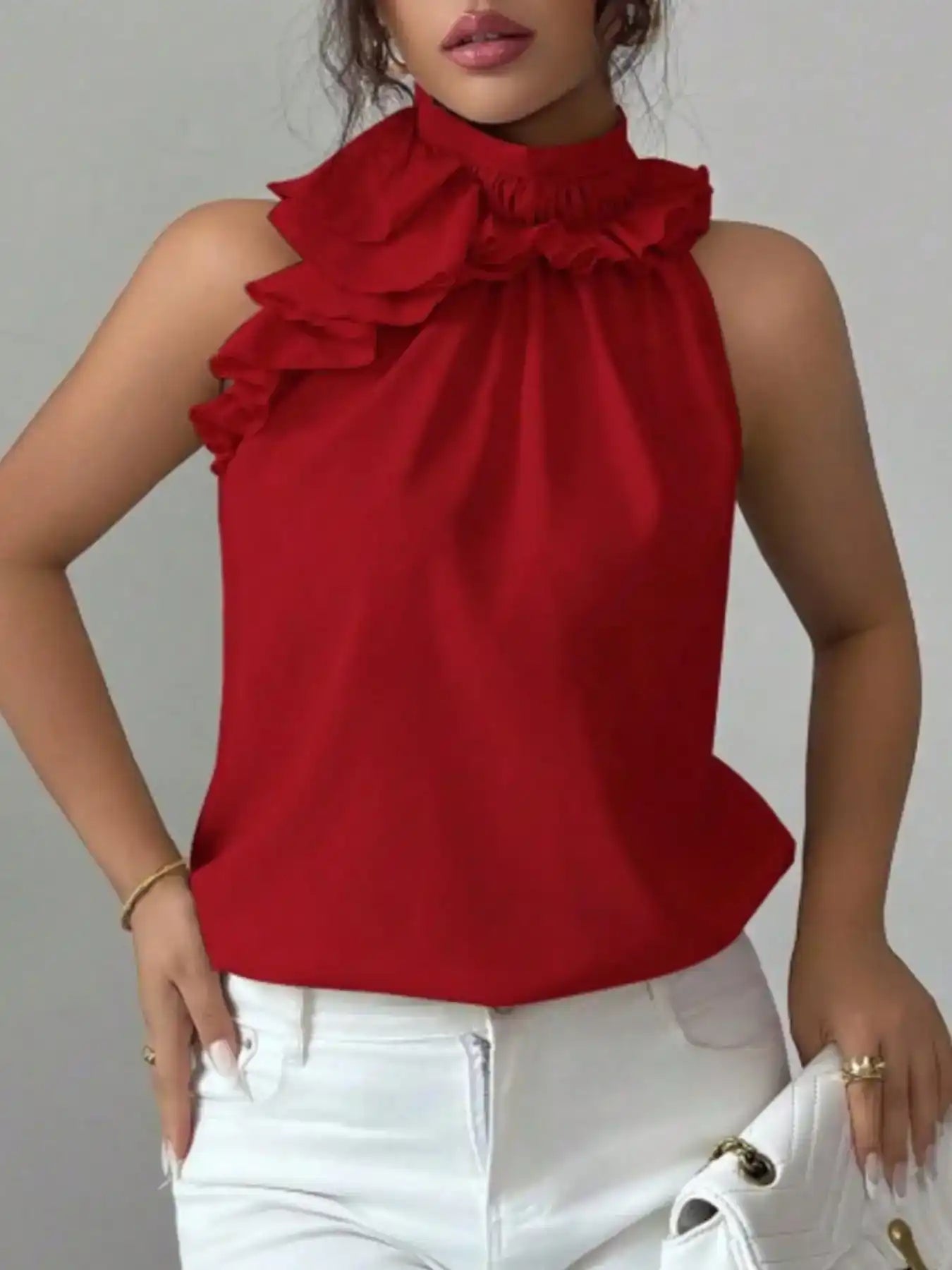 Woman wearing a sleeveless red ruffle blouse with high neck and white jeans