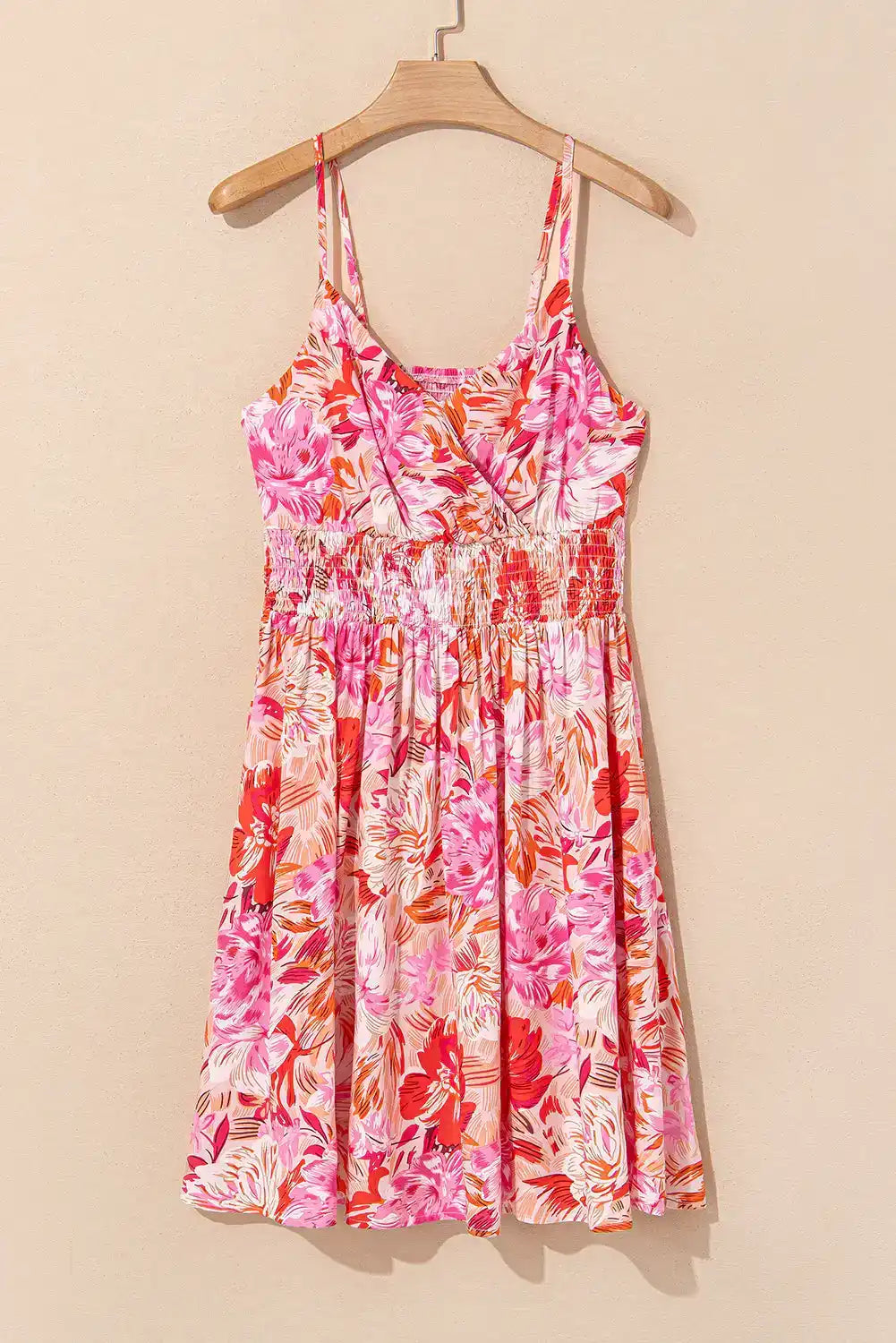 Pink and red floral sundress with spaghetti straps and smocked waist, hanging on a hanger.
